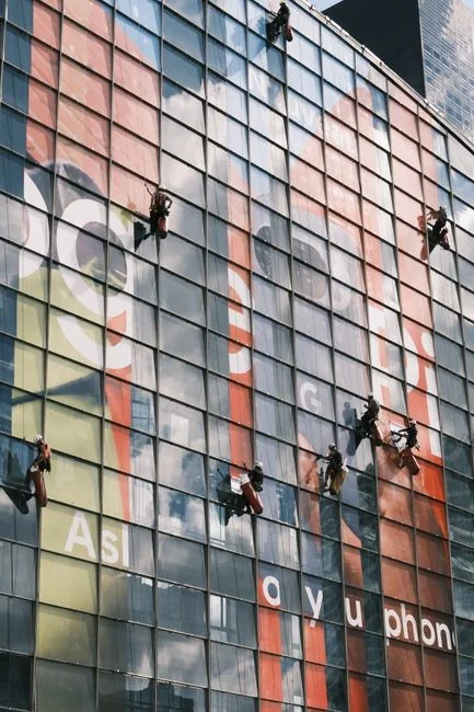 Close-up of hand cleaning window with squeegee outdoors using yellow gloves.